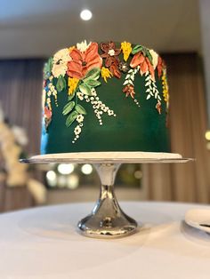 a green cake with flowers on it sitting on top of a white tablecloth covered table