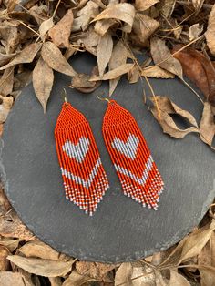 two orange and white beaded earrings sitting on top of a stone slab next to leaves