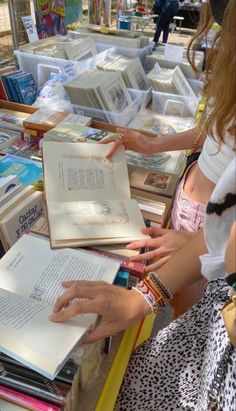 two girls are reading books at an outdoor book market, one is wearing a white shirt and the other has a black polka dot skirt