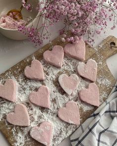 heart shaped cookies on a cutting board with powdered sugar and flowers in the background