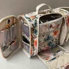 an open floral bag sitting on top of a white table next to another bag filled with pens and pencils