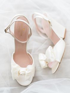 a pair of white shoes with bows on the toes and heels are sitting on a bed