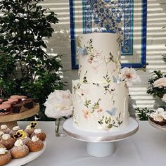 a white cake with flowers on it sitting next to cupcakes and other pastries