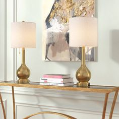 a table with two lamps on it in front of a painting and a bookcase