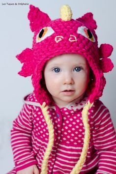 a baby wearing a pink knitted hat with a dragon on it's head