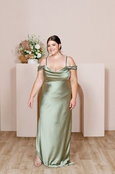 a woman in a silver dress standing on a wooden floor next to a vase with flowers