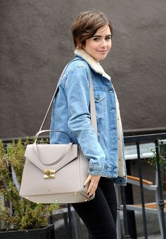 a woman in black pants and a denim jacket carrying a beige purse with a fur collar