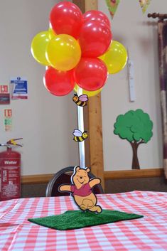 winnie the pooh balloon centerpiece on top of a table with red and yellow balloons