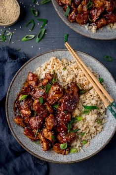 two plates filled with rice and chicken next to chopsticks on a table top