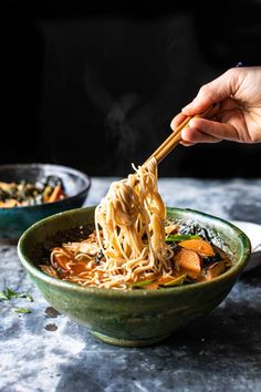 someone holding chopsticks over a bowl of noodles