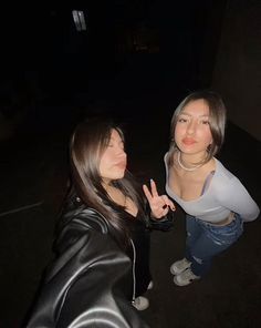 two women standing next to each other with one making the peace sign while the other holds her hand up