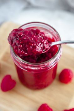 raspberry jam in a glass jar with two spoons on the table next to it