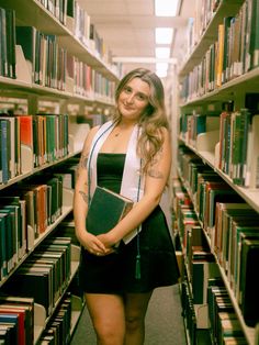 a woman standing in front of a library filled with books and holding a binder