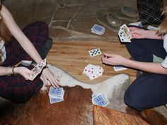 three women playing cards on the floor in front of a cow's skin,