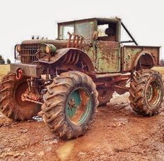 an old, rusty truck with large wheels sits in the mud