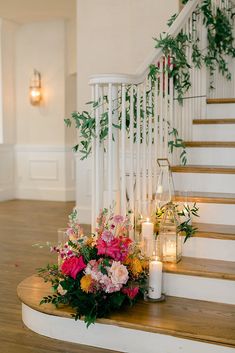 flowers and candles are on the stairs in front of an open staircase case with greenery