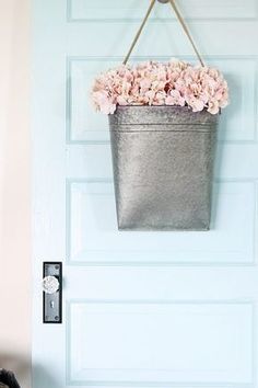 a metal bucket filled with pink flowers hanging on a blue door