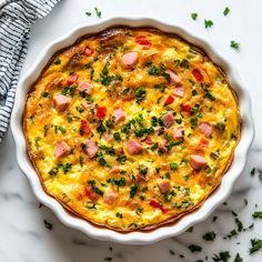 an omelet with ham and cheese in a white dish on a marble surface