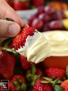 a hand holding a strawberry with cream cheese on it and strawberries in the background