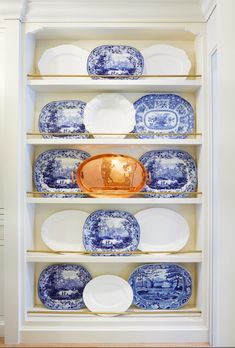 blue and white plates are on shelves in a room with wood flooring, along with a gold plate