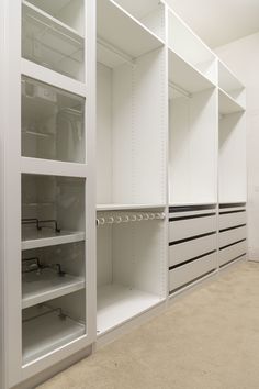 an empty walk in closet with lots of white shelves and shelving unit doors open