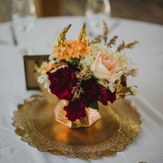 a vase filled with flowers sitting on top of a gold plate next to wine glasses