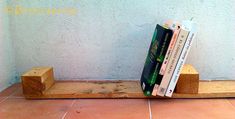 three books are sitting on a wooden shelf next to a blue wall and tile floor