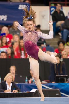 a woman in a purple leotard doing a trick on the balance beam while people watch