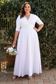 a woman standing in front of a fence wearing a white dress