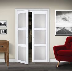 a red chair sitting in front of a white door next to a wooden table with pictures on it