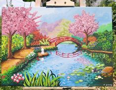 an easel with a painting of a bridge over a river and flowers on it