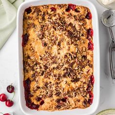 a casserole dish with cherries and nuts on top, next to spoons