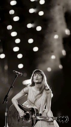 a woman holding a guitar while standing in front of a microphone