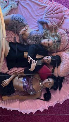 three women laying on a pink bed with their reflection in the mirror's wall