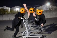 three people wearing pumpkin faces pushing a shopping cart with their hands up in the air