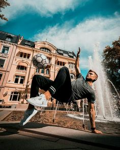 a man doing a handstand in front of a fountain with a soccer ball on his head