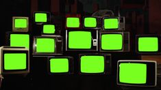 many old televisions with green screen are stacked on top of each other in the dark