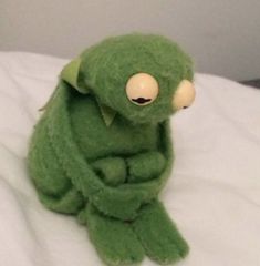 a green stuffed animal sitting on top of a bed