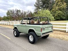 an old pick up truck is parked on the side of the road in front of a white fence