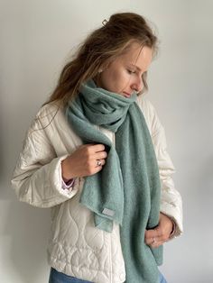 a woman wearing a white jacket and blue jeans is holding a green scarf in her hands