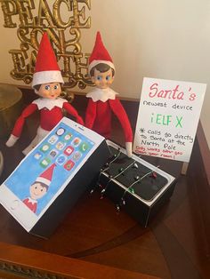 two elfs sitting next to an electronic device on a table with a sign that says santa's telef x