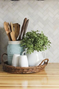 a basket filled with kitchen utensils sitting on top of a counter next to a potted plant