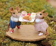 two little mice that are standing on a table with food and drink in their hands