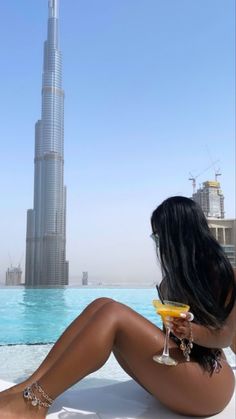 a woman sitting on the edge of a swimming pool with a drink in her hand