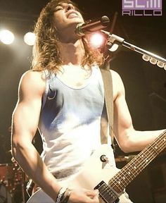 a man with long hair holding a guitar and singing into a microphone