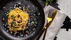 a black plate topped with pasta and nuts on top of a table next to silverware