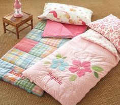 a child's bed with pink comforter and pillows on the floor next to a small table