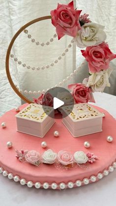 a pink cake decorated with roses and two small boxes