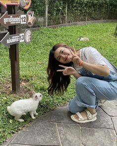 a woman kneeling down next to a small white rabbit near a sign with directions on it