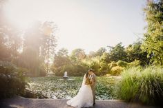 a bride and groom standing in front of a pond